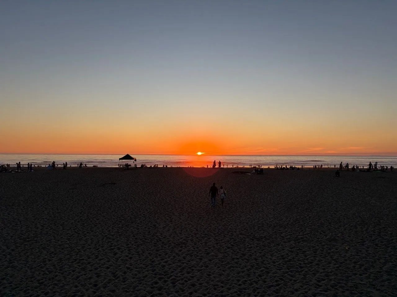 Orange sunset over the ocean with people on the beach