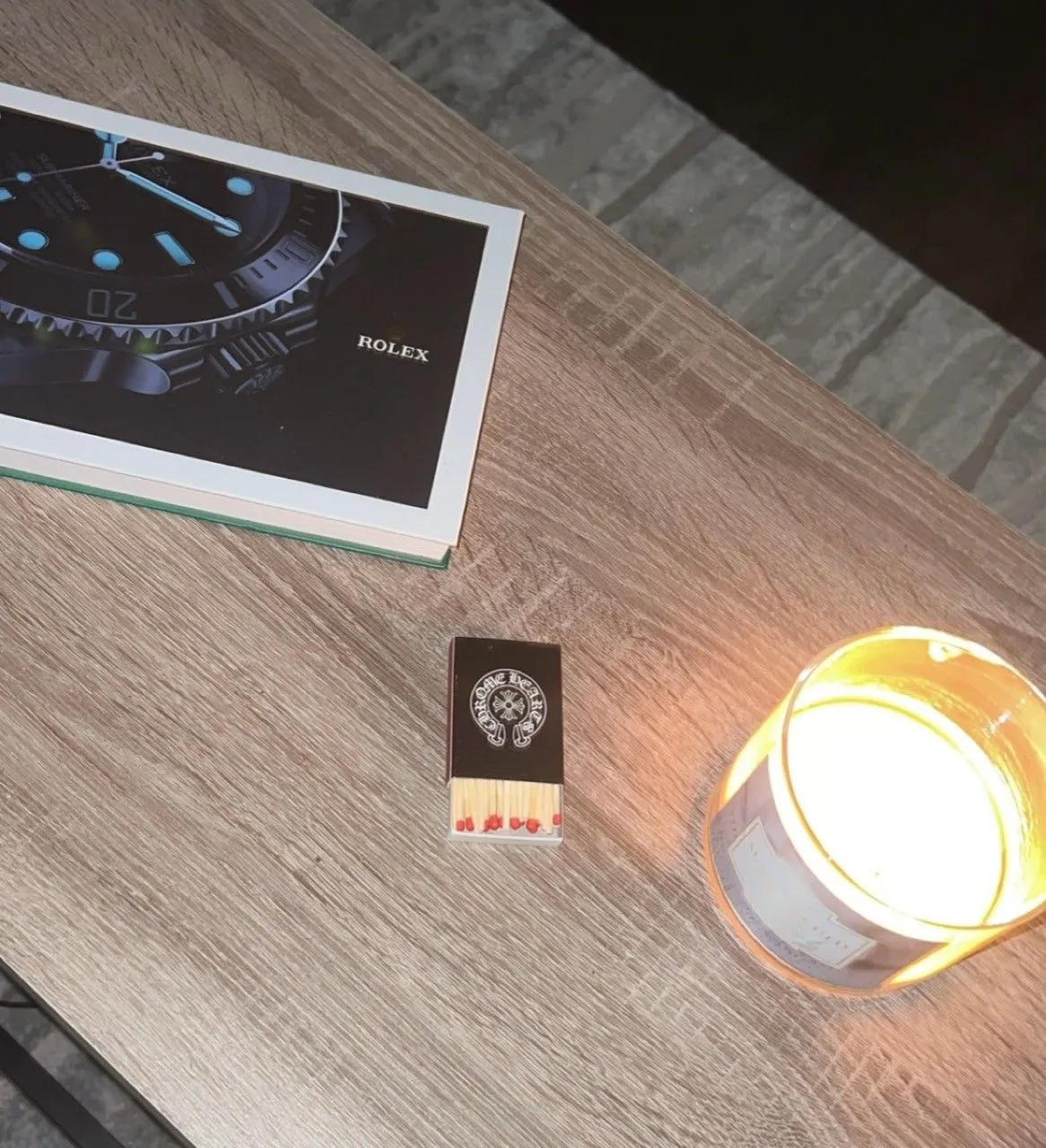 A candle, matchbook, and watch book on a wooden table